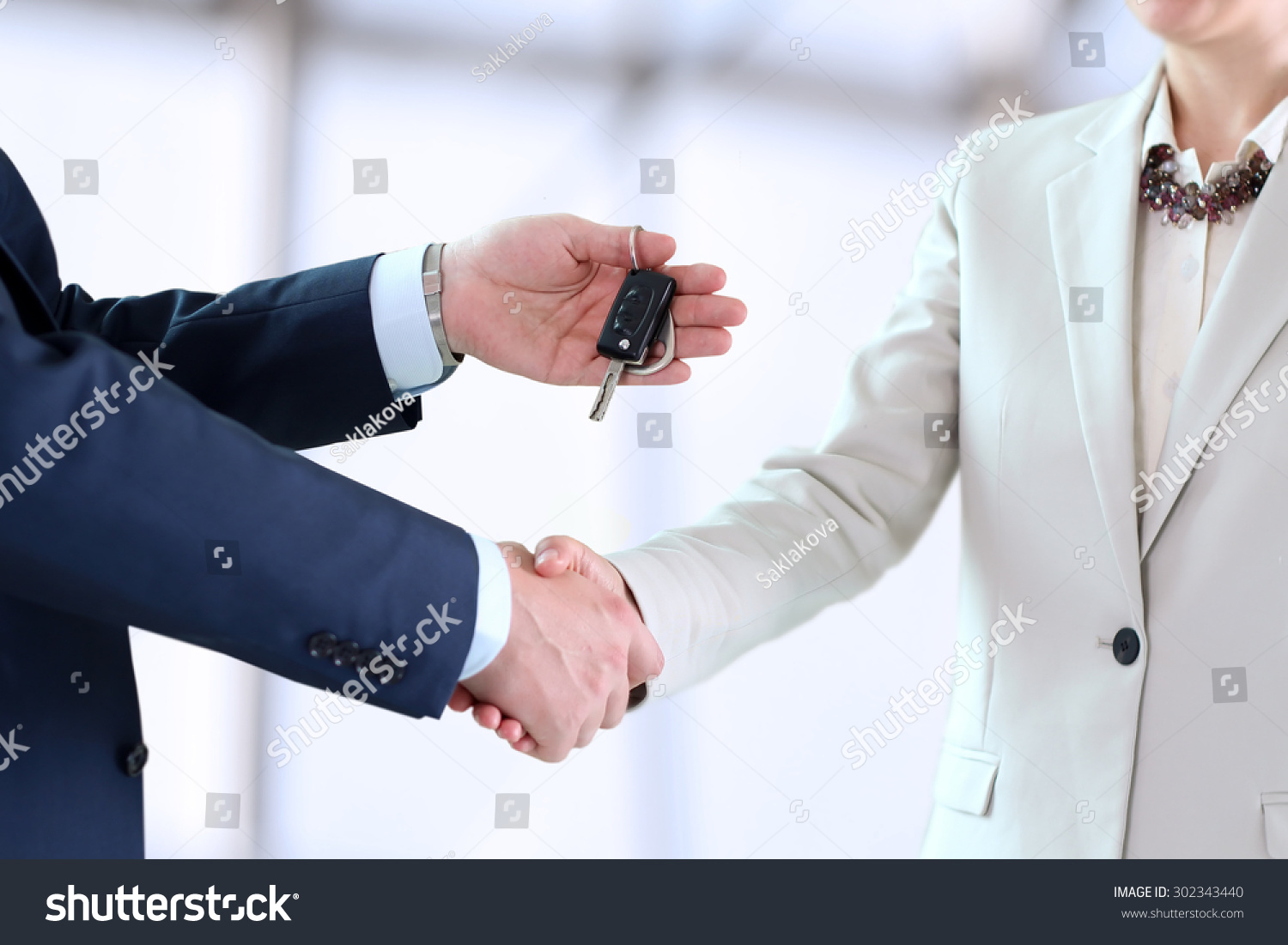 Car saleswoman handing over the keys for a new car to a young businessman . Handshake between two business people