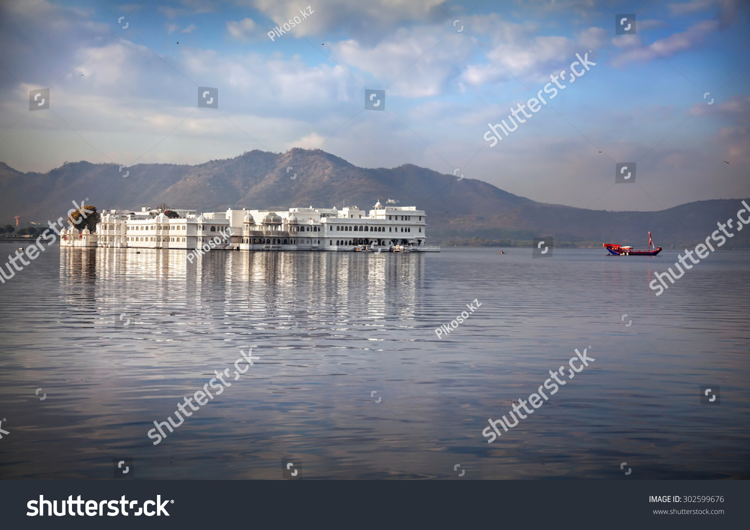 White palace and boat on Lake Pichola at cloudy sky in Udaipur  Rajasthan  India