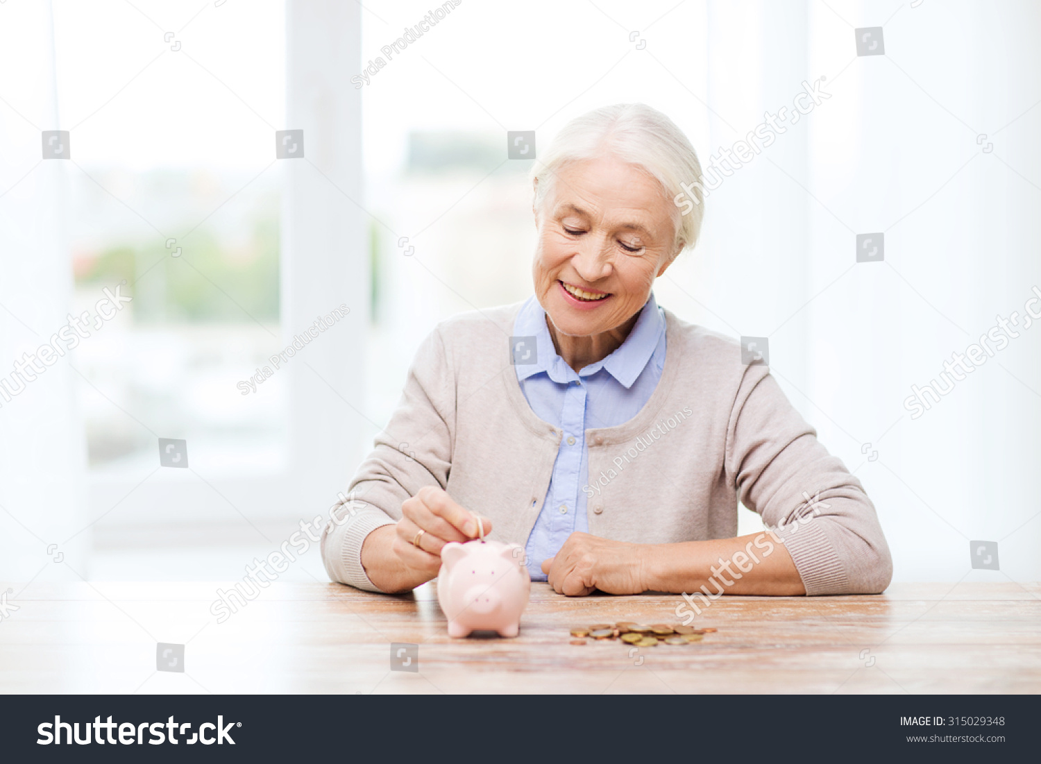 savings money annuity insurance retirement and people concept - smiling senior woman putting coins into piggy bank at home