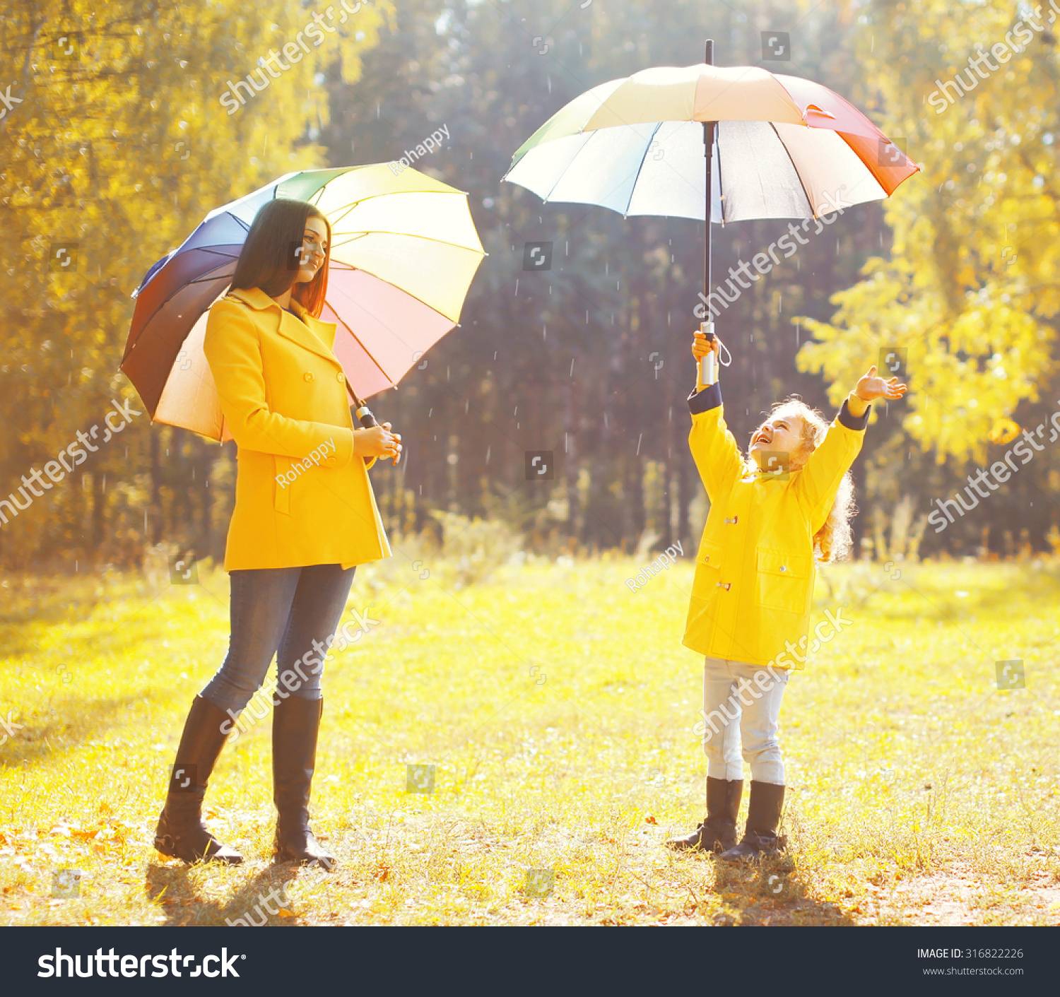 Happy family with umbrellas in sunny autumn rainy day  mother and child enjoying rain