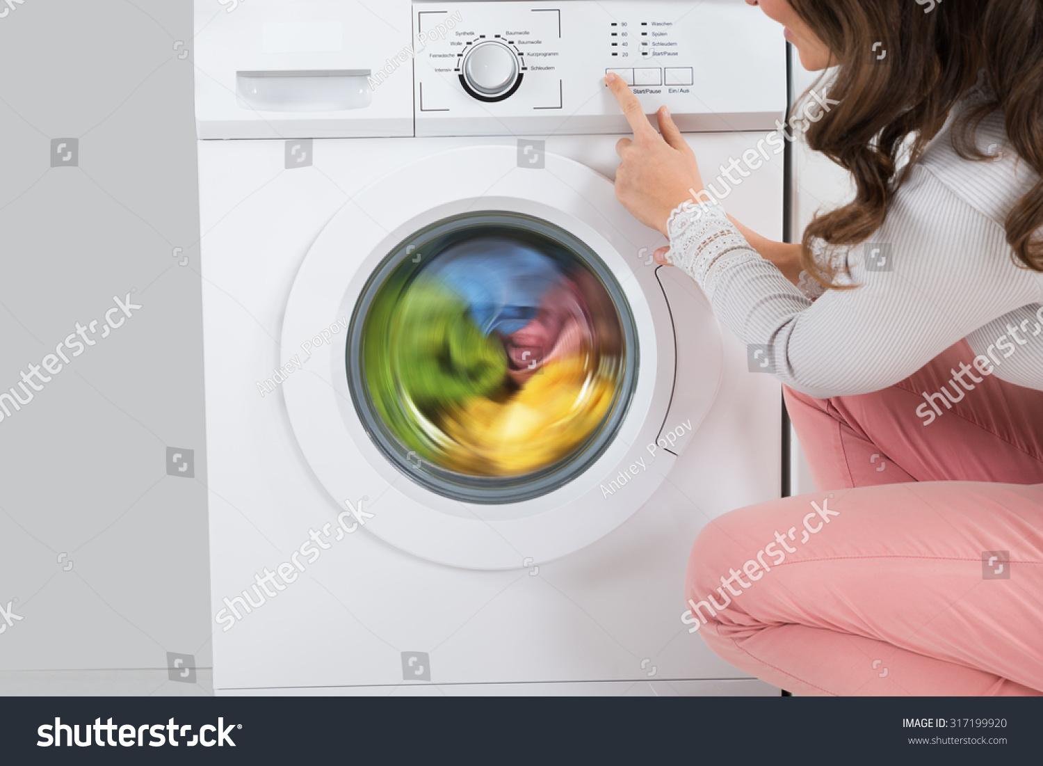 Close-up Of Young Woman Pressing Button Of Washing Machine In Kitchen