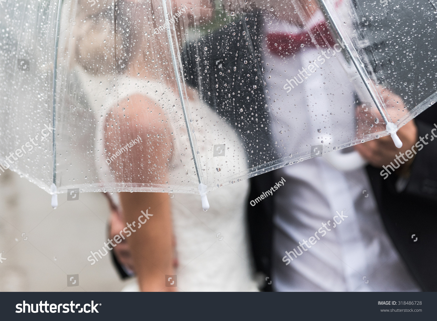 the bride and groom in the rain are covered with a transparent umbrella  rain drops