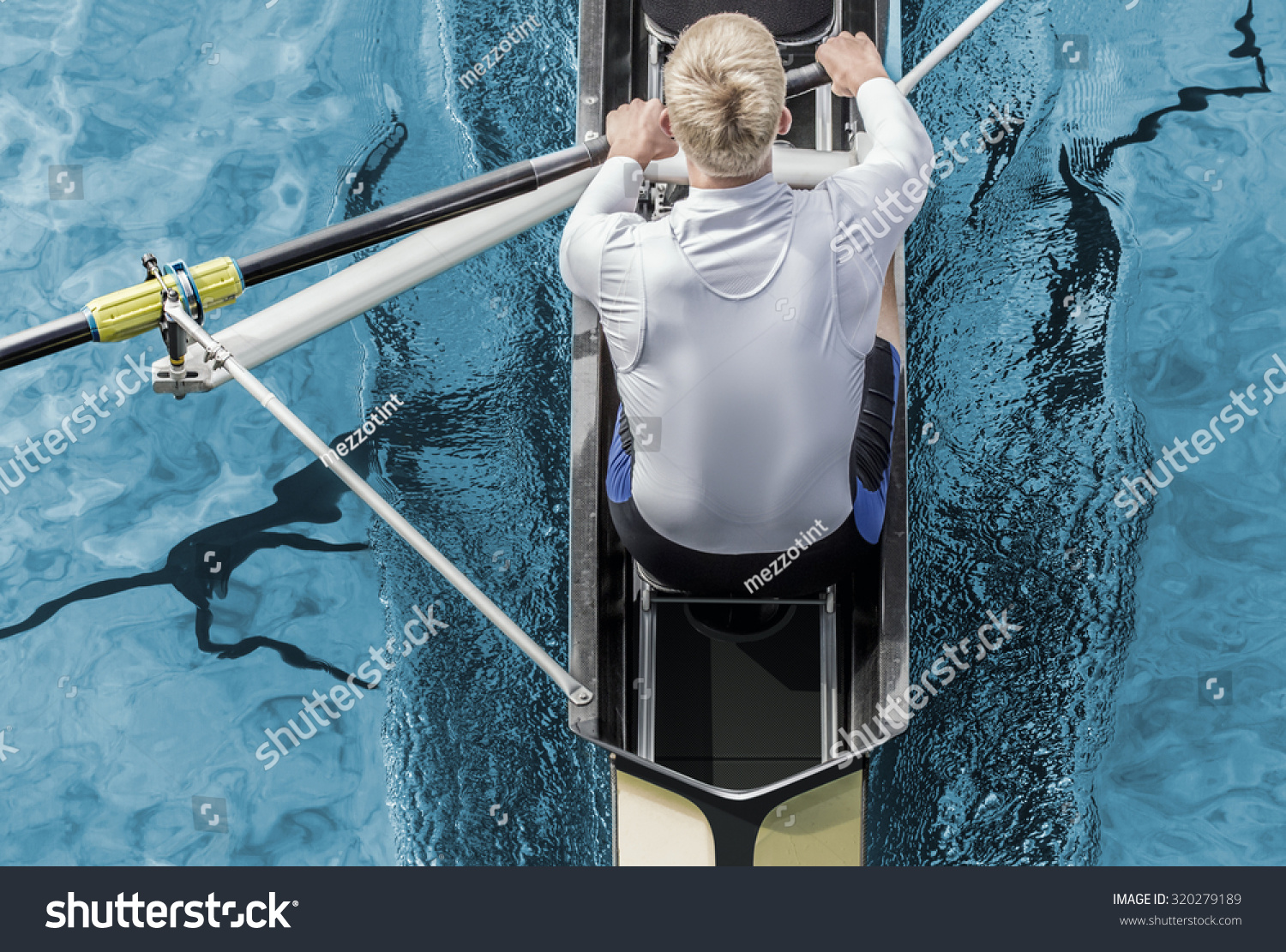 Top view of athletic competition rower who strokes his paddle through metallic blue water.