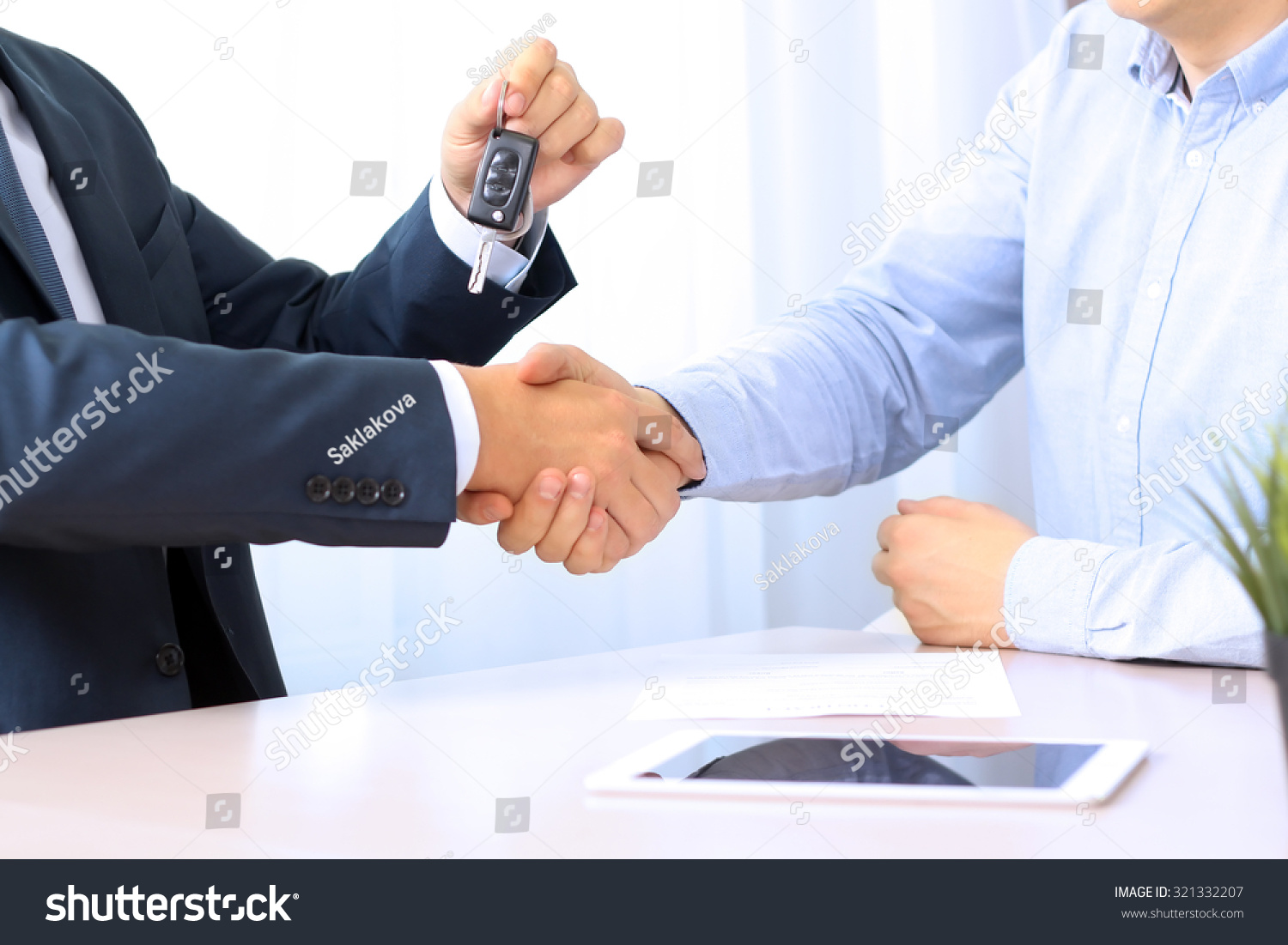 Car salesman handing over the keys for a new car to a young businessman . Handshake between two business people. Focus on a key