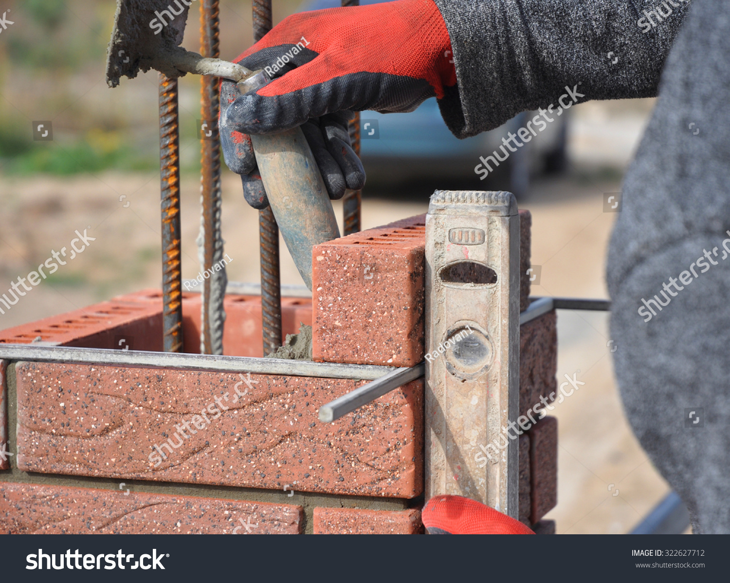 Bricklayer Worker Installing Red Clinker Blocks and Caulking Brick Masonry Joints Exterior Wall with Trowel putty Knife and Fixing with Spirit Level Outdoor