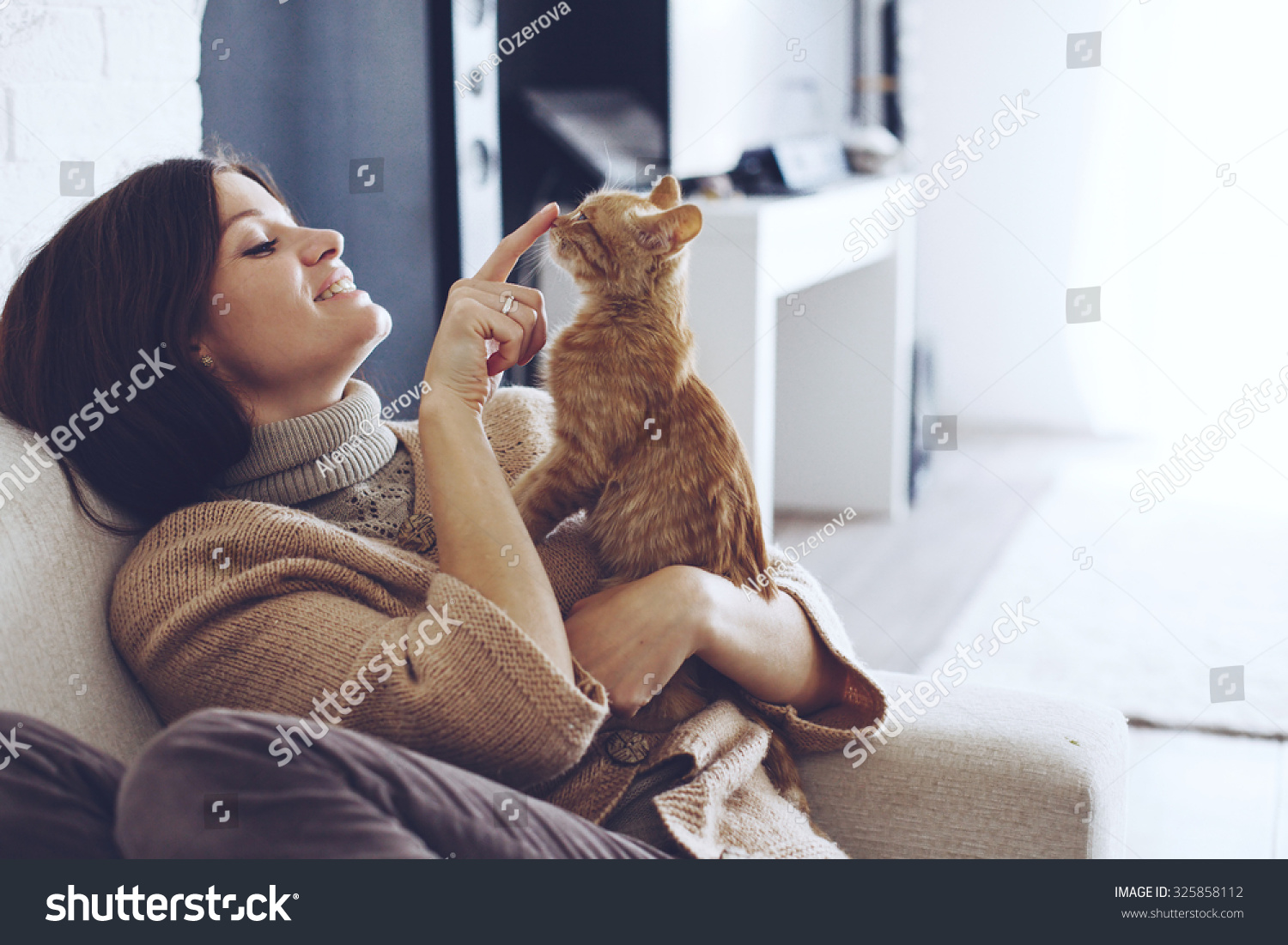 Young woman wearing warm sweater is resting with a cat on the armchair at home one autumn day