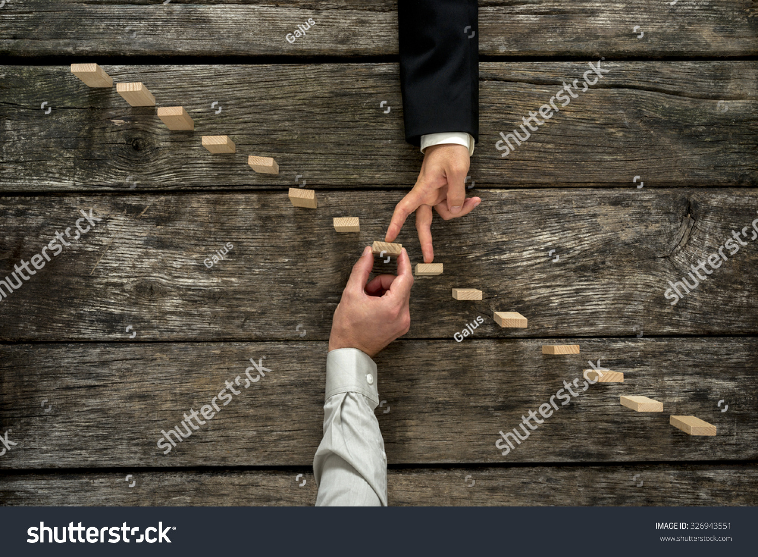 Conceptual image of business partnership and support - businessman supporting wooden step in a staircase made of pegs as his partner walks his fingers up towards growth  achievement and development.
