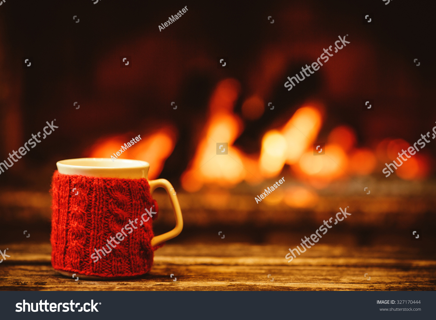 Cup of hot drink in front of warm fireplace. Holiday Christmas concept. Mug in red knitted mitten standing near fireside. Cozy relaxed magical atmosphere in a chalet.