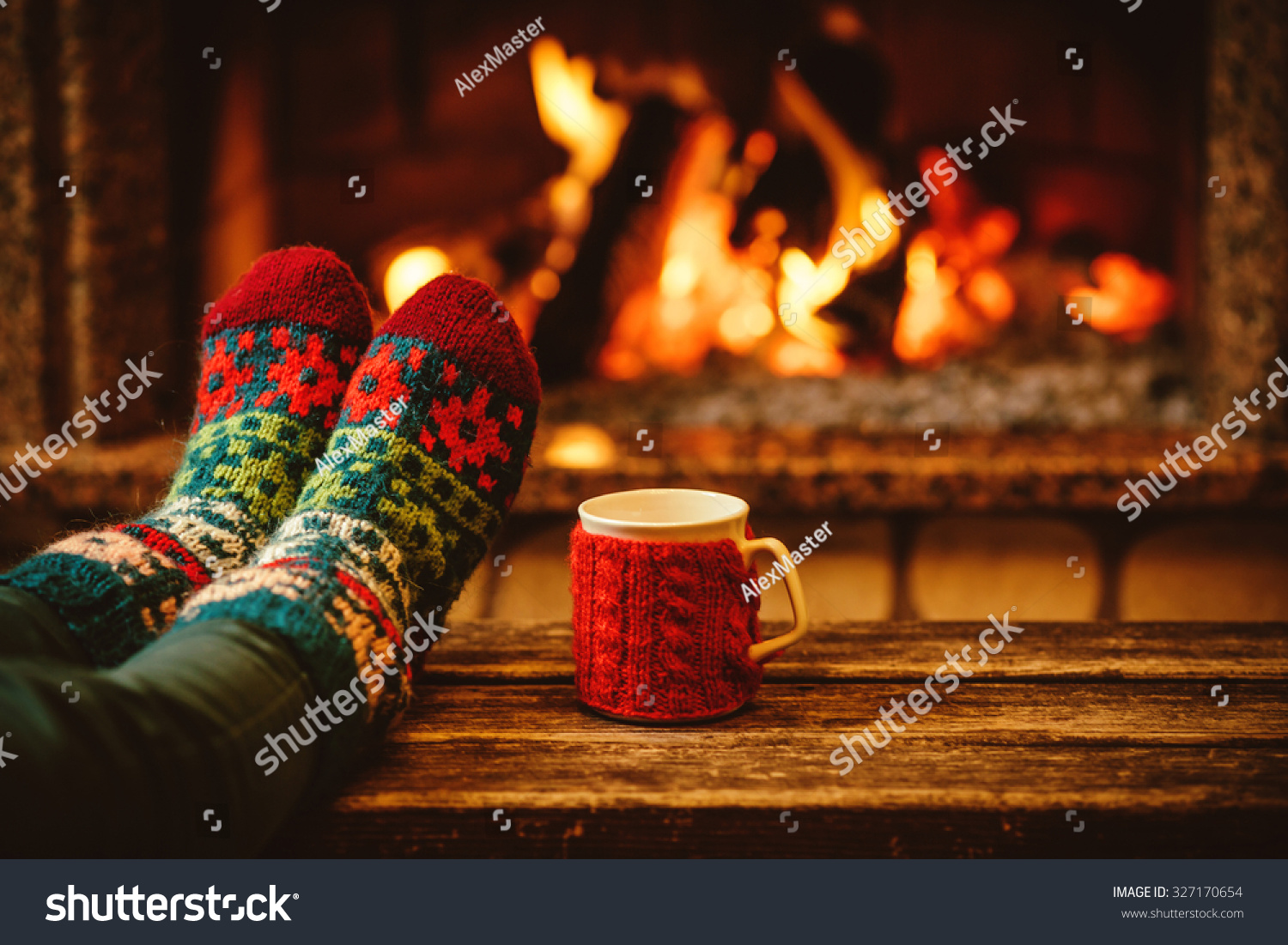 Feet in woollen socks by the Christmas fireplace. Woman relaxes by warm fire with a cup of hot drink and warming up her feet in woollen socks. Close up on feet. Winter and Christmas holidays concept.