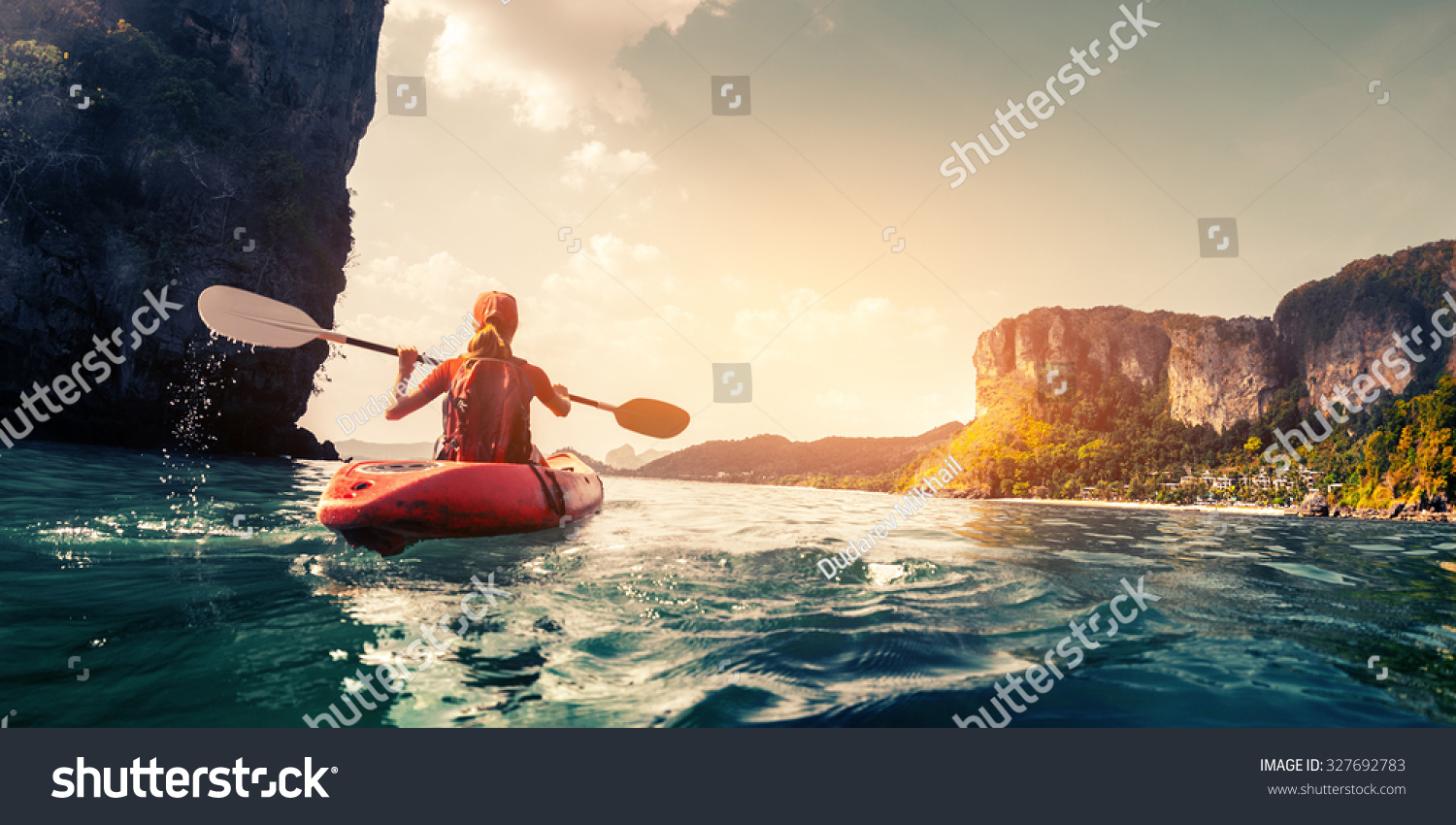 Lady paddling the kayak in the calm tropical bay at sunset