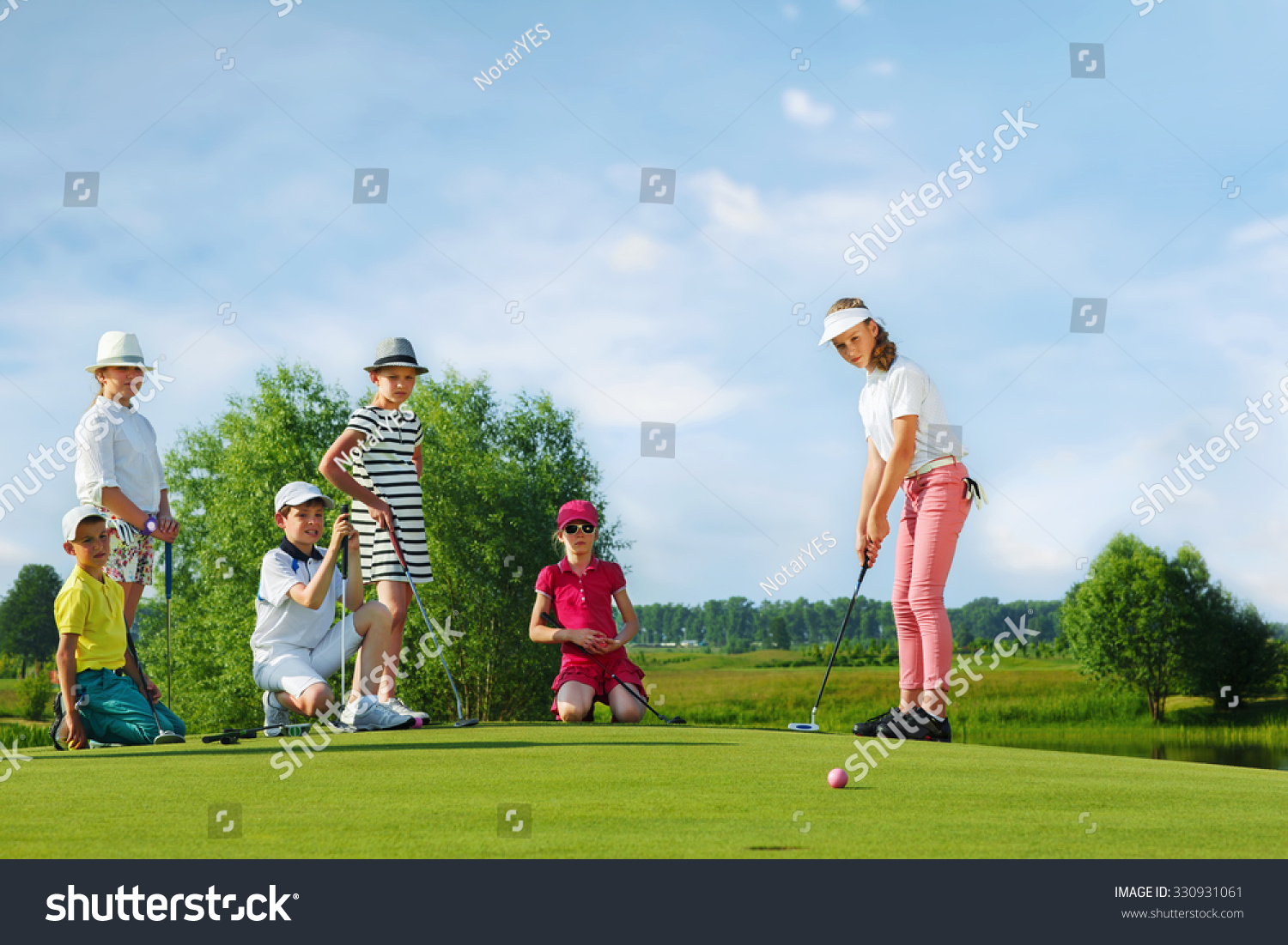 Kids playing golf by putter on green
