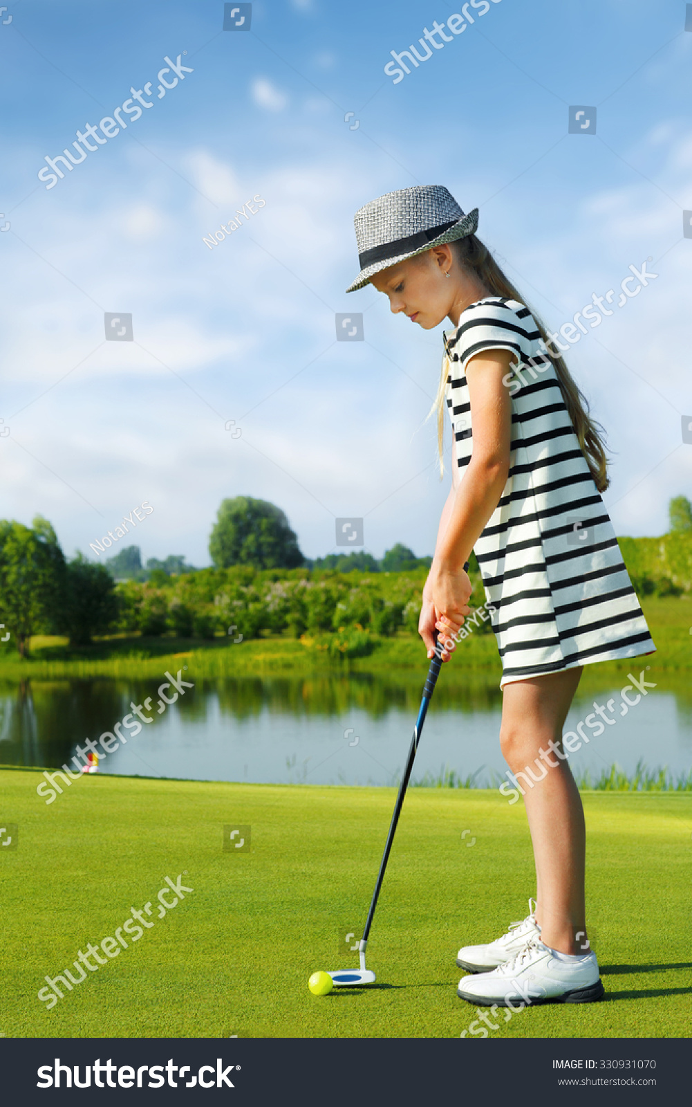 Girl playing golf and hitting by putter on green
