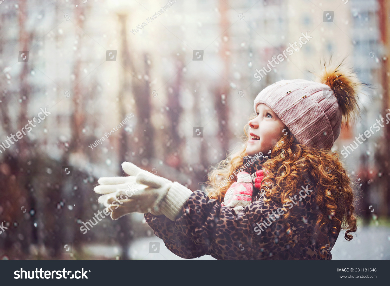 Cute little girl stretches her hand to catch falling snowflakes. First snow. Toning instagram filter.