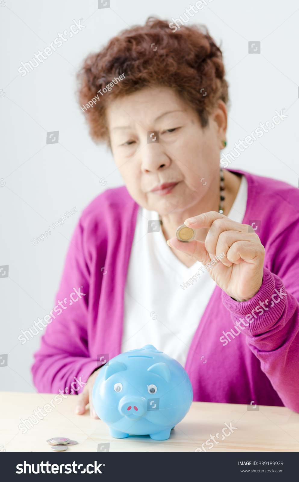 savings money annuity insurance retirement and people concept - smiling senior woman putting coins into piggy bank at home