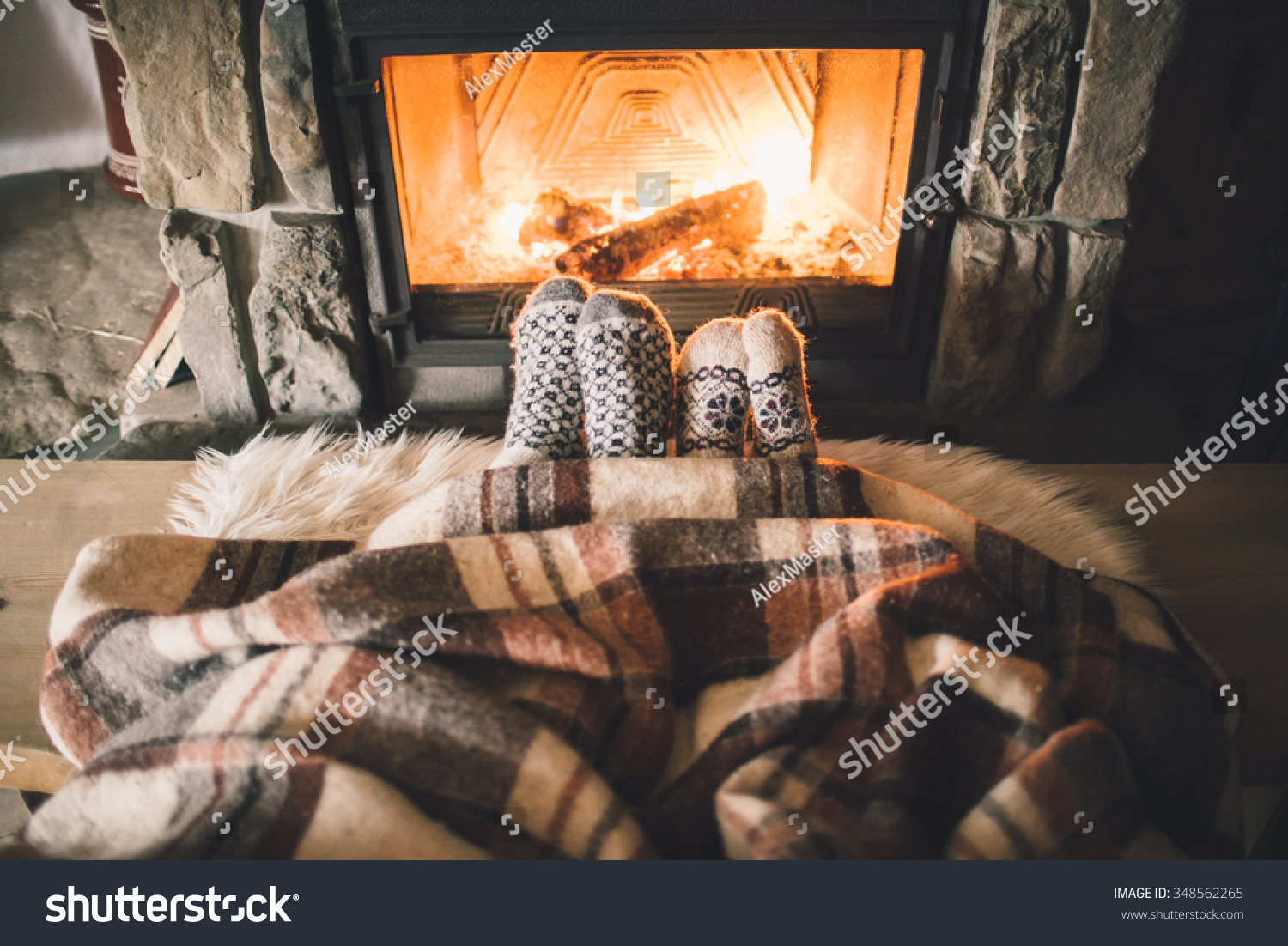Feet in woollen socks by the Christmas fireplace. Couple sitting under the blanket relaxes by warm fire and warming up their feet in woollen socks. Winter and Christmas holidays concept.