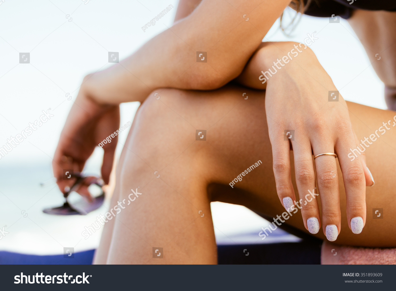 Woman in a swimsuit sits on the coast  in her hand sunglasses. Close-up. Warm colors.