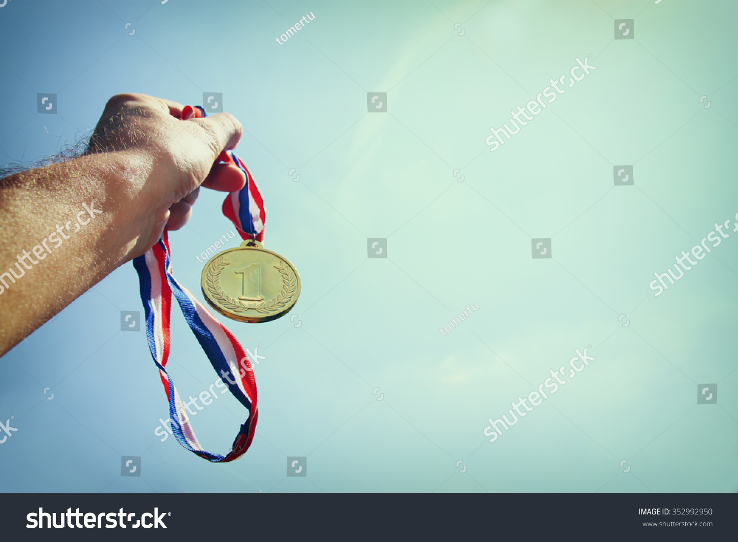 man hand raised  holding gold medal against Sky. award and victory concept. selective focus. retro style image.