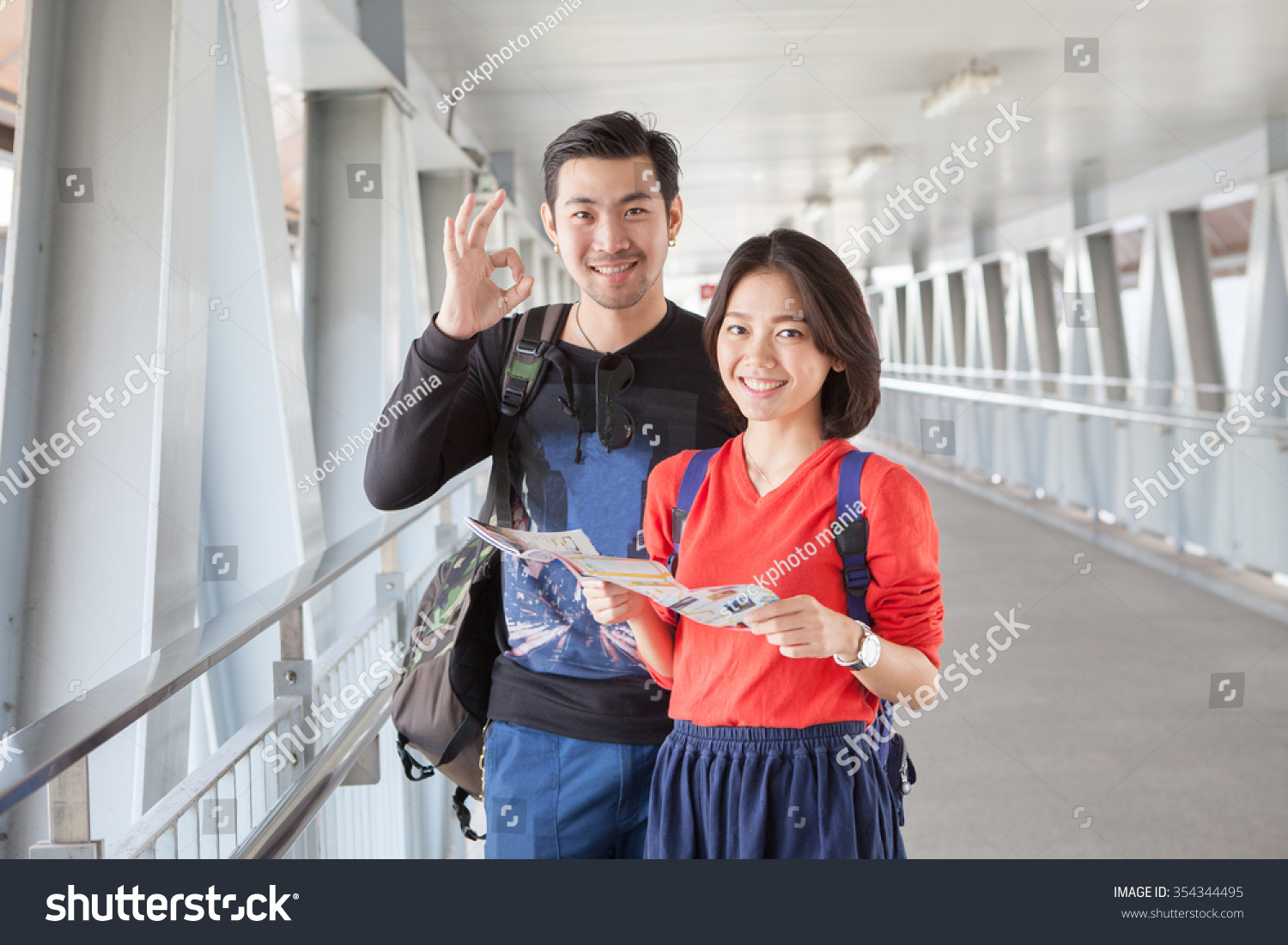  asian traveling man and woman standing with toothy smiling face with guide book in hand