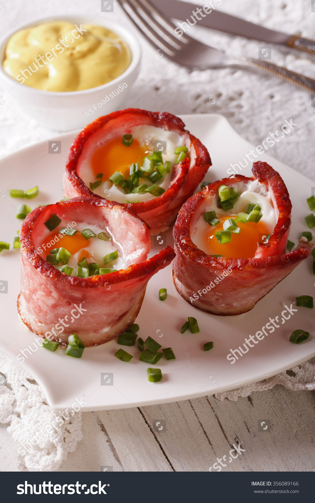 Fried eggs wrapped in crispy bacon on a plate and sauce on the table. vertical