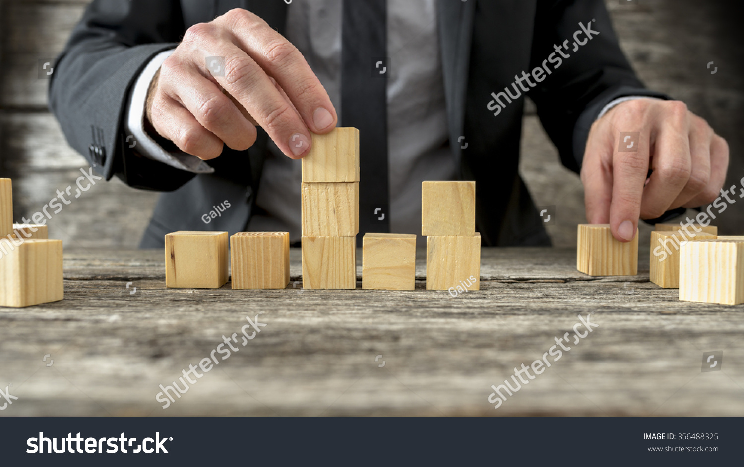 Concept of business strategy and planning - front view of male hand placing and positioning wooden blocks in various structures.