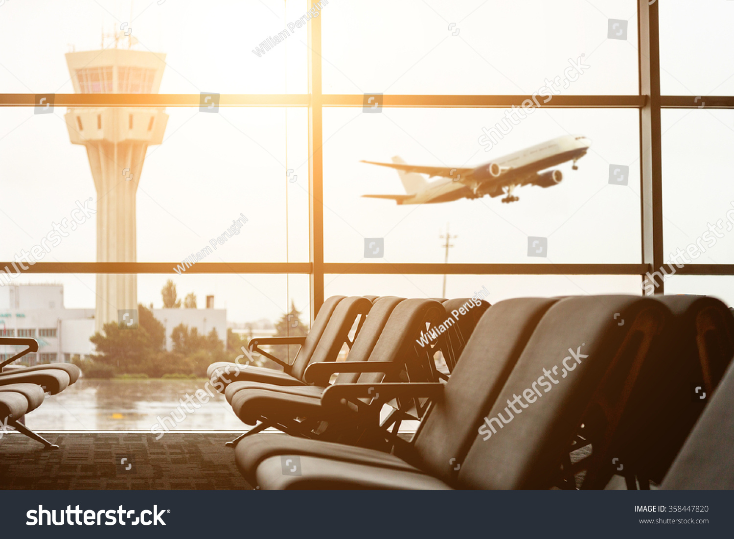 Empty chairs in the departure hall at airport with the control tower and an airplane taking off at sunset. Travel and transportation concepts.