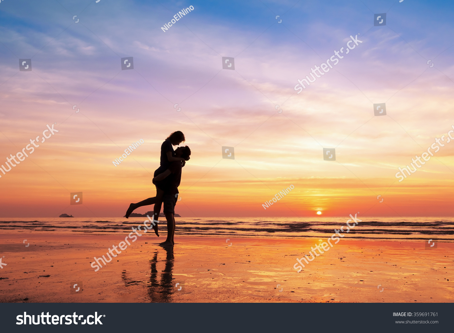 Couple kissing on the beach with a beautiful sunset in background  man lifting the woman