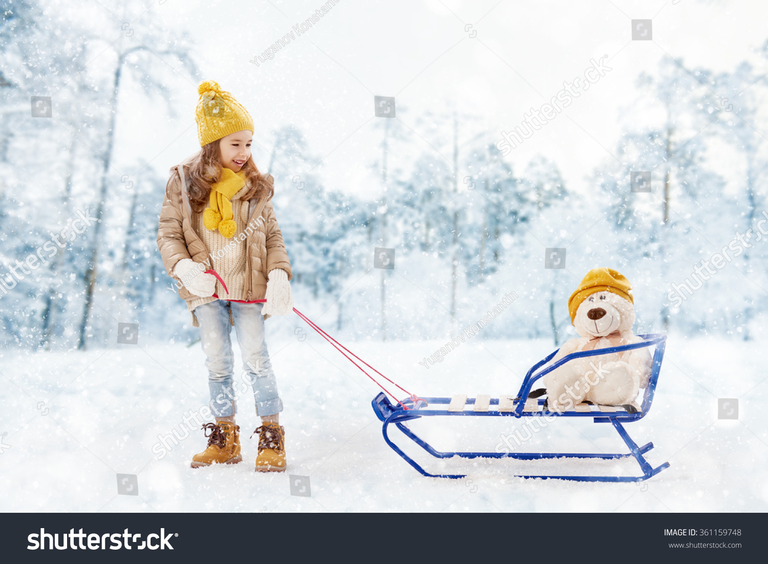 happy child girl plaing with a toy on a snowy winter walk. child rolls a teddy bear on a sled