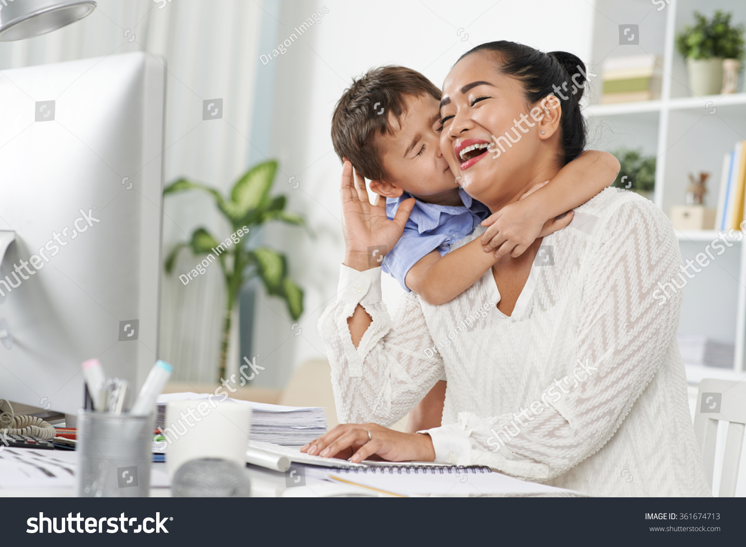 Little Indonesian boy kissing his mom  who is working in office