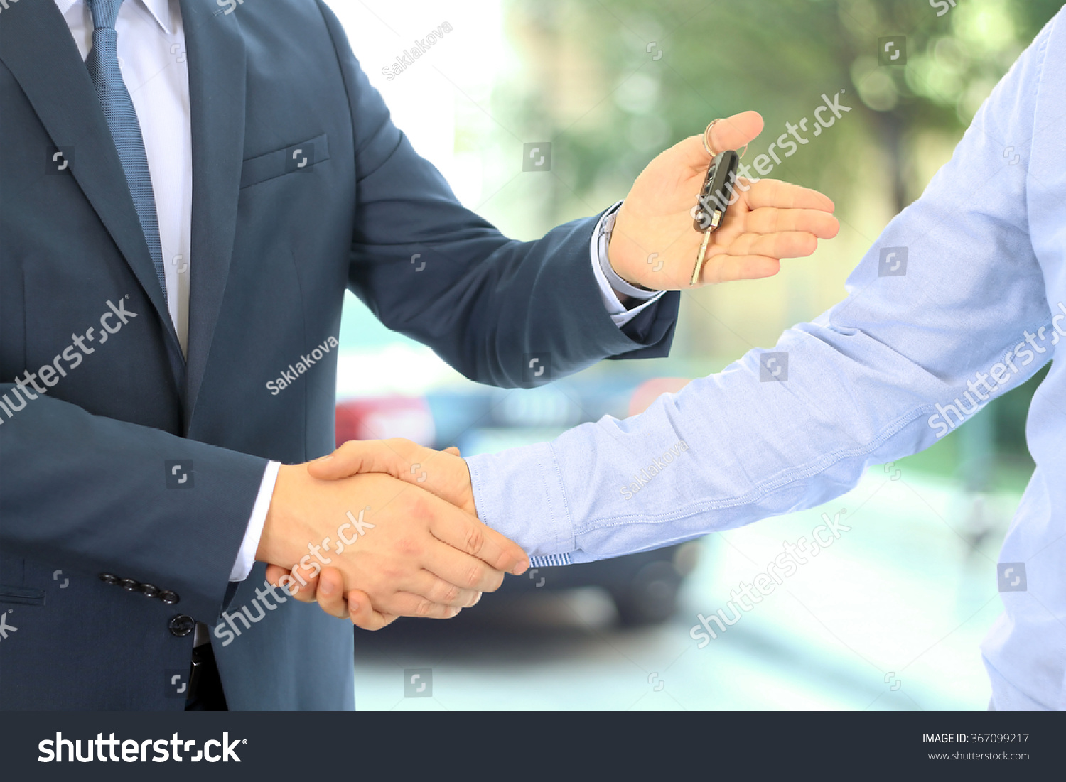 Car salesman handing over the keys for a new car to a young businessman . Handshake between two business people. Focus on a key