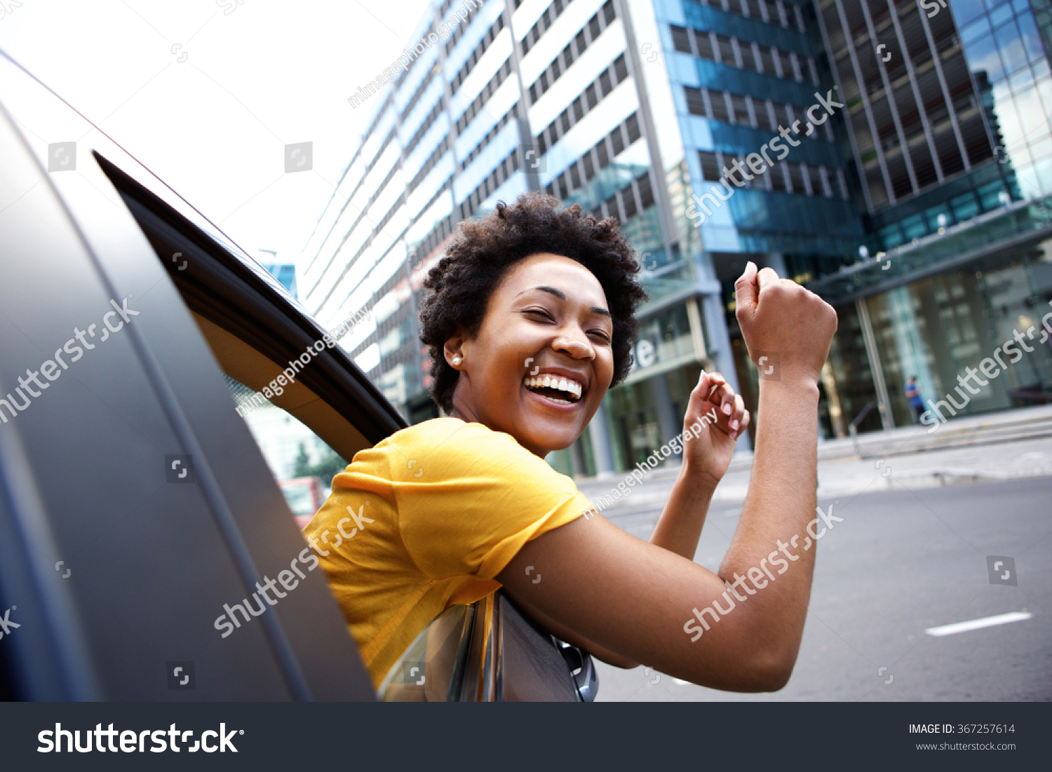 Portrait of cheerful young african woman looking out the car window with her arms raised
