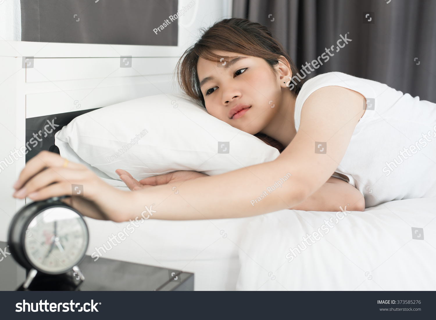 Asain woman waking up and turning off the alarm clock