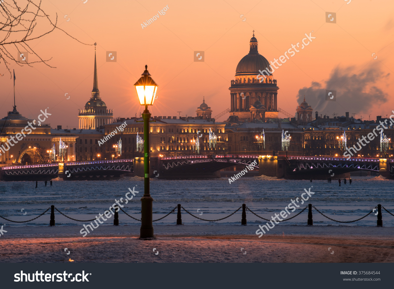 View of the evening city decorated with lights. In the foreground a street light. In the background the main attractions - the Palace Bridge and St. Isaac sobo. Russia Saint-Petersburg.