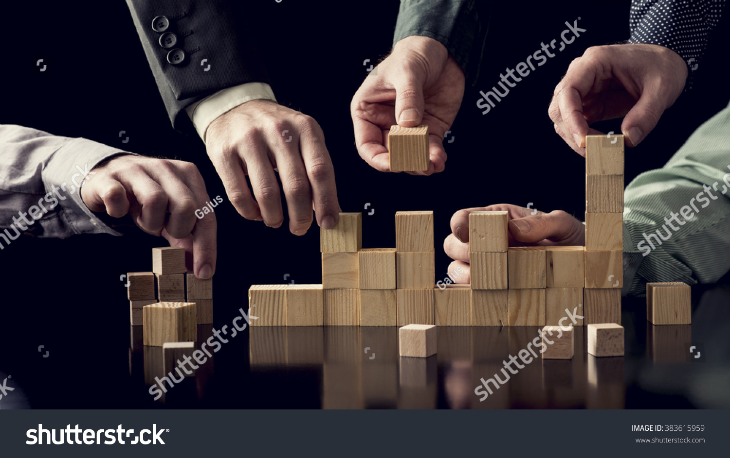 Teamwork and cooperation concept - five male hands building a structure of wooden blocks on black desk with reflection  toned retro effect.