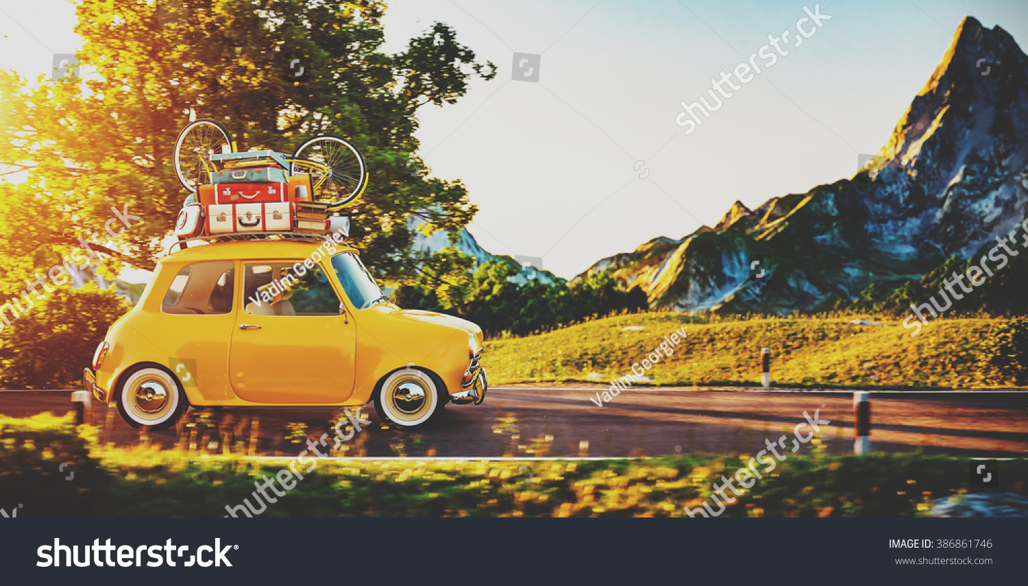 Cute little retro car with suitcases and bicycle on top goes by wonderful countryside road at sunset