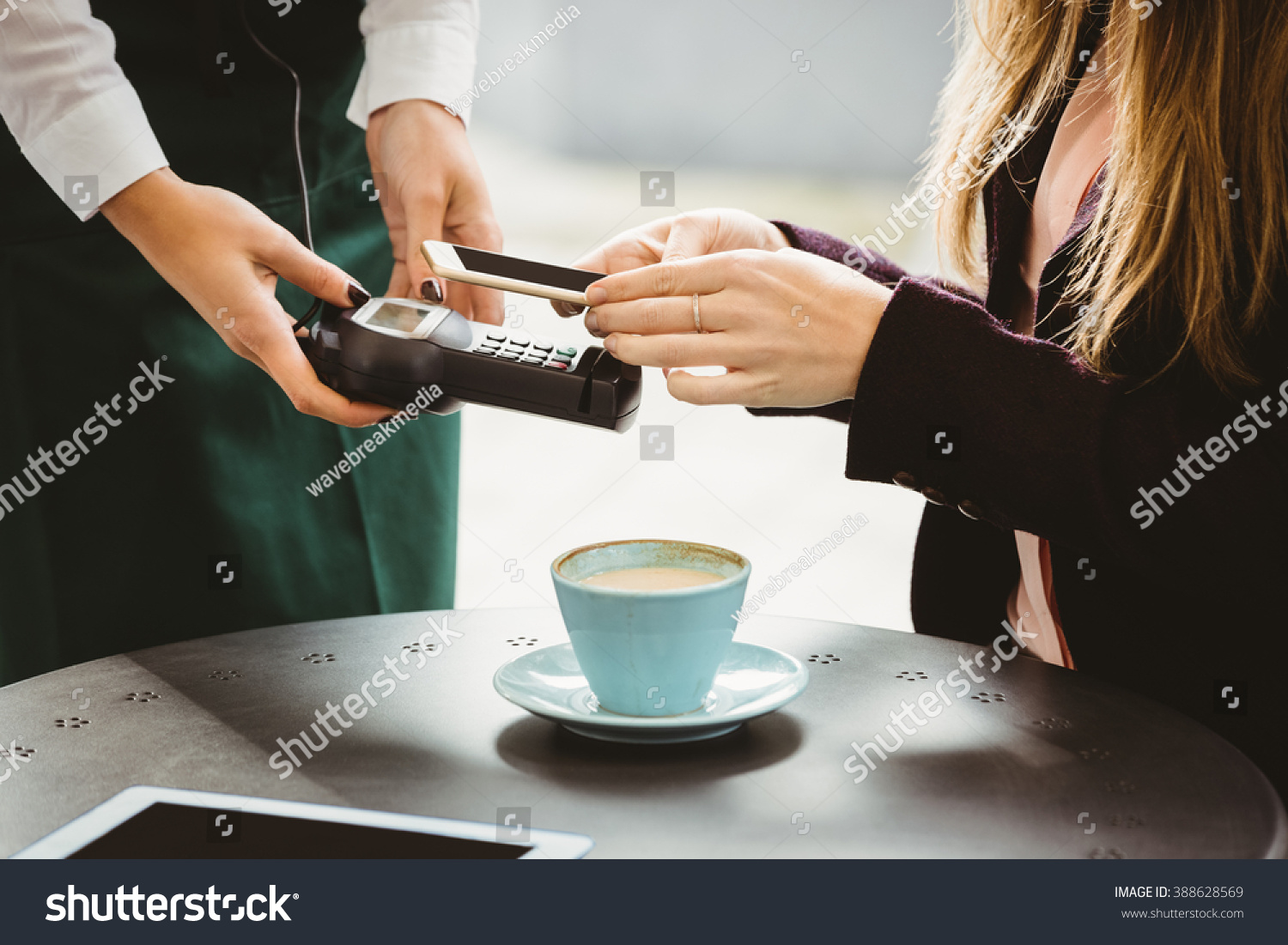 Woman paying with mobile phone in cafe