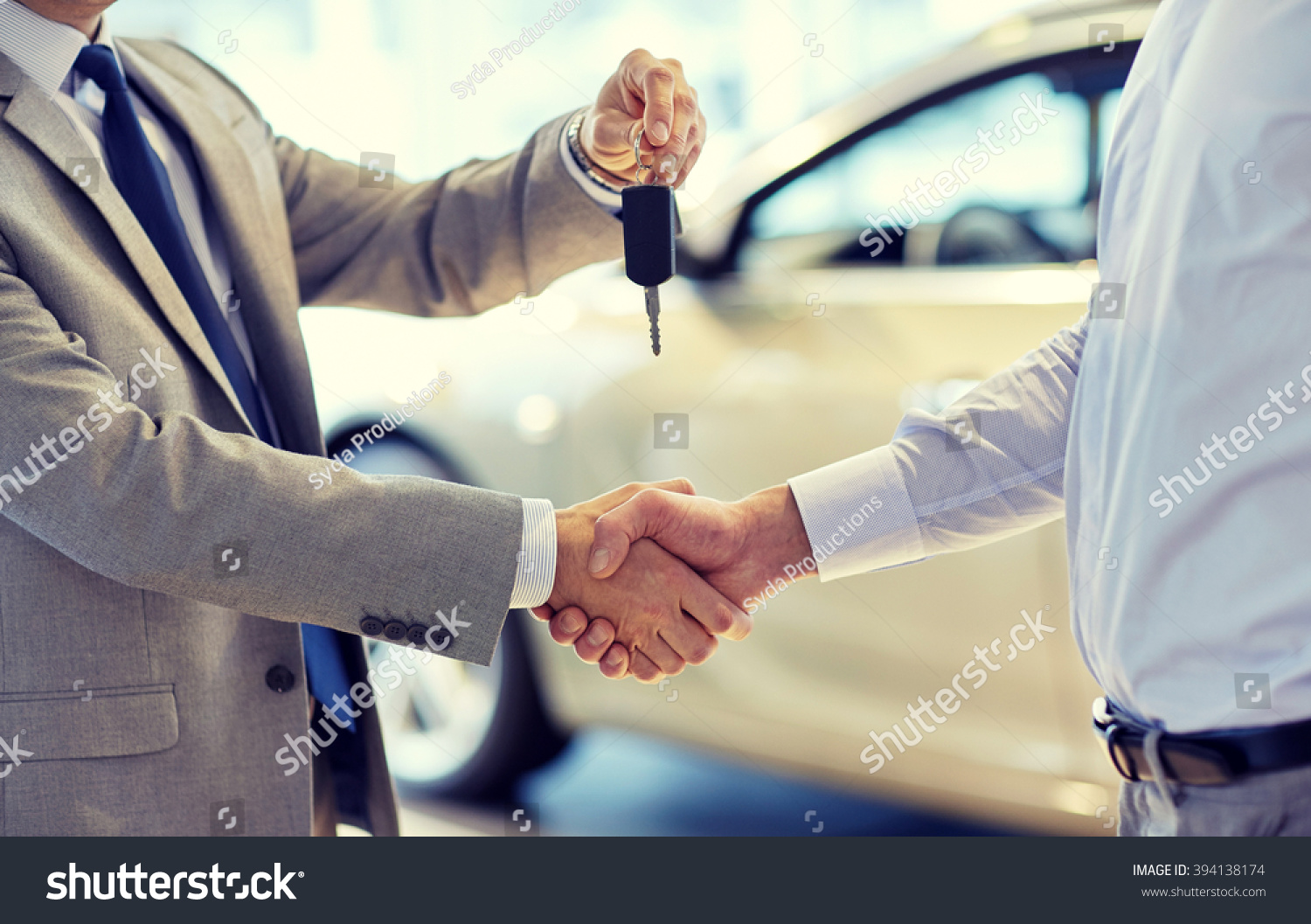 auto business car sale deal gesture and people concept - close up of dealer giving key to new owner and shaking hands in auto show or salon
