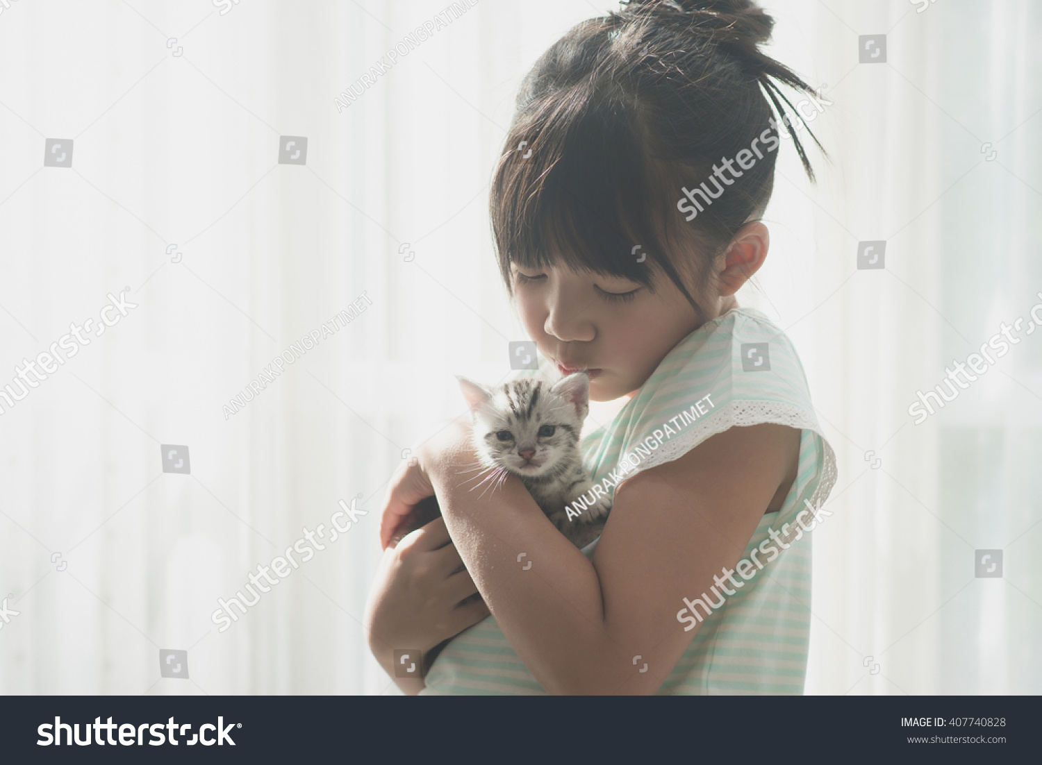 Beautiful asian girl kissing american shorthair cat under sunlight from a window