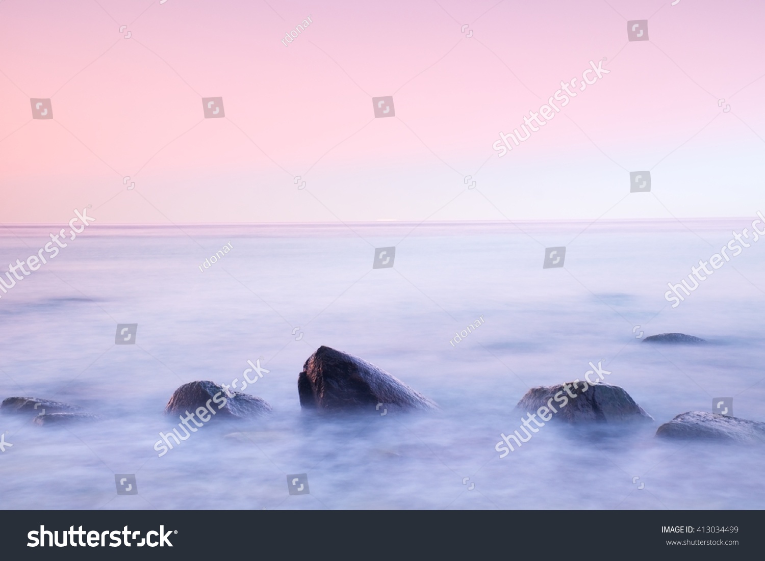 Romantic atmosphere in peaceful morning at sea. Big boulders sticking out from smooth wavy sea. Pink horizon with first hot sun rays.