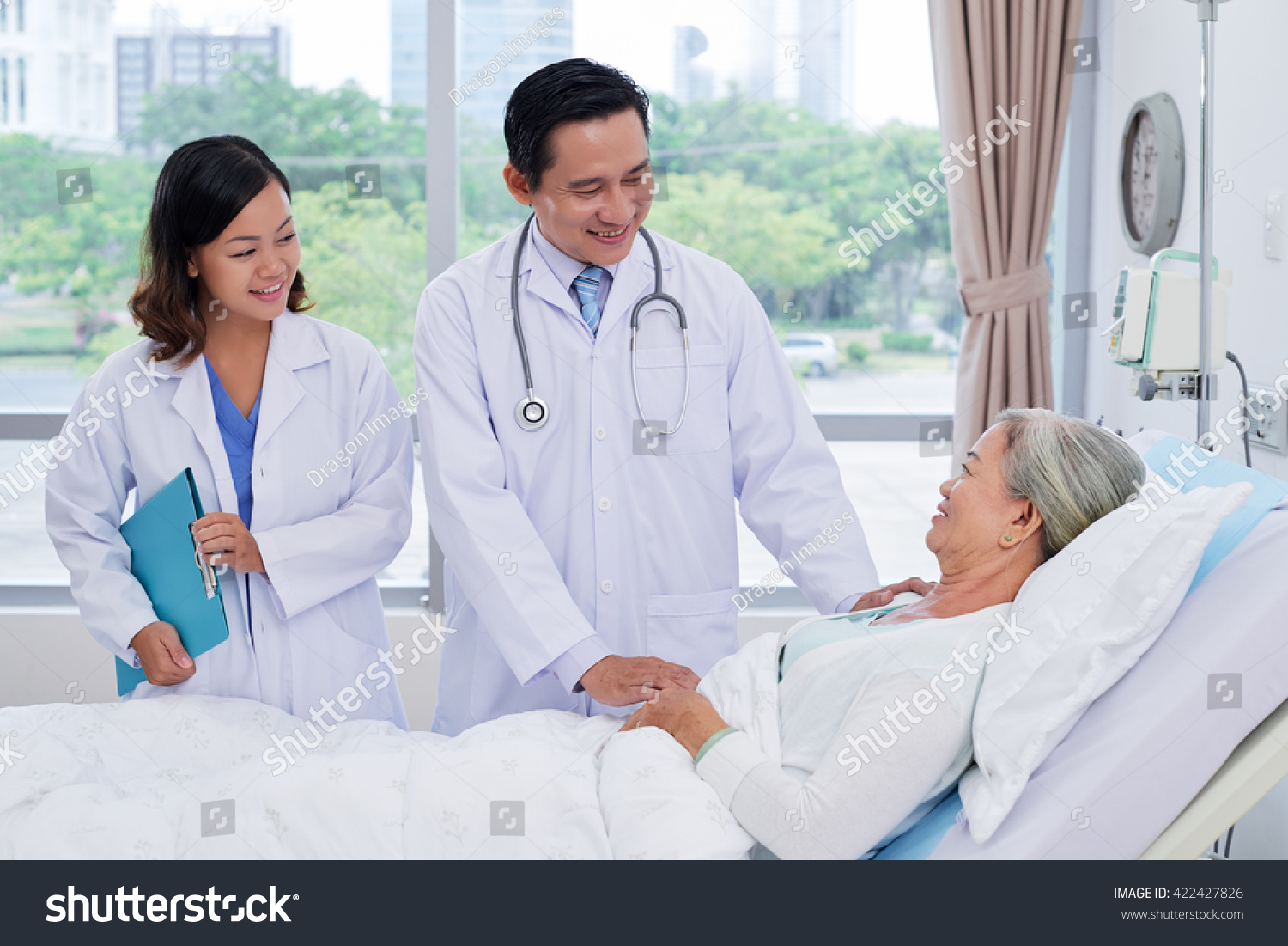 Vietnamese doctor and nurse talking to senior patient in ward