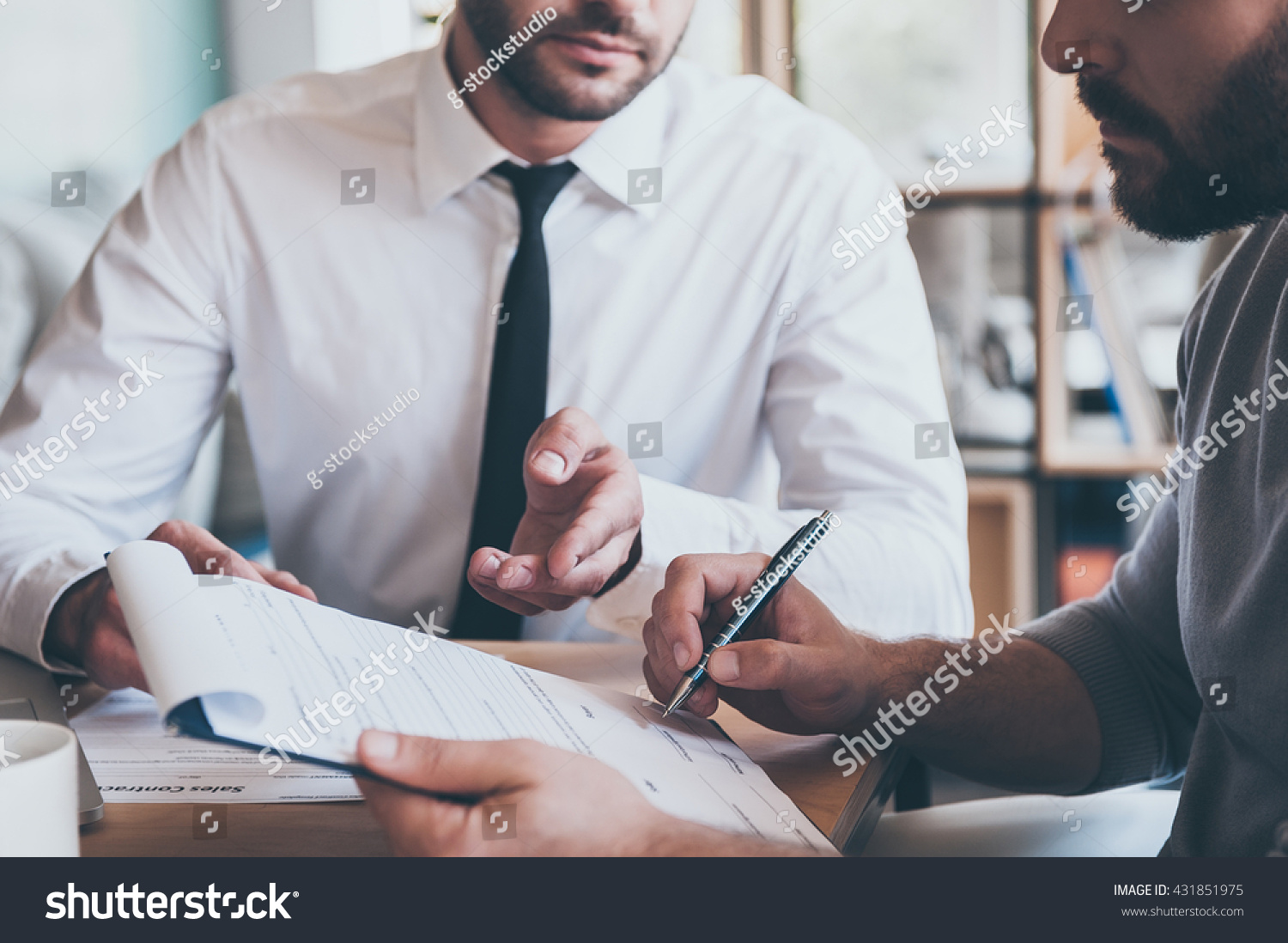Signing contract. Close-up of confident young man signing some document while another man in shirt and tie sitting close to him and pointing document