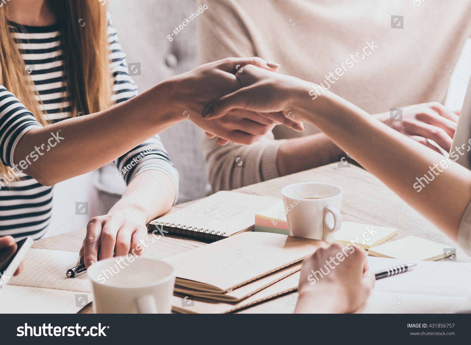 Sealing a deal. Close-up of two businesswomen shaking hands while sitting at the desk with man in the background
