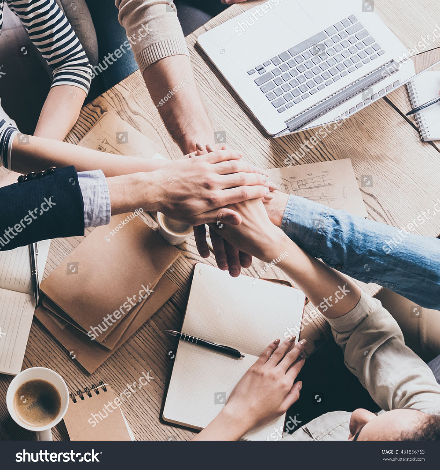 Unity is a key to success. Top view of people holding hands together while sitting at the wooden desk together