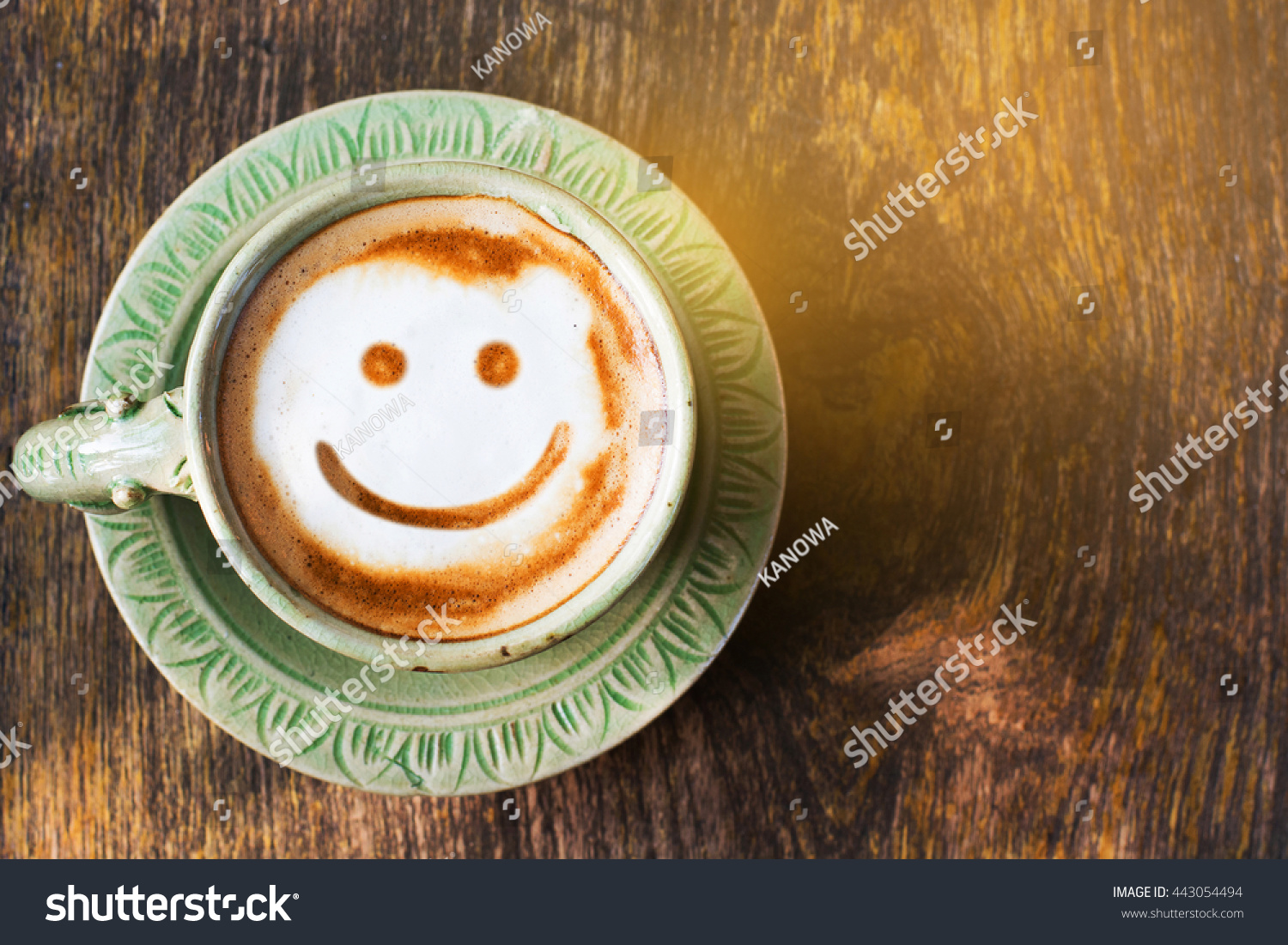 Smile of latte coffee with sunshine on wooden background.(Top view)