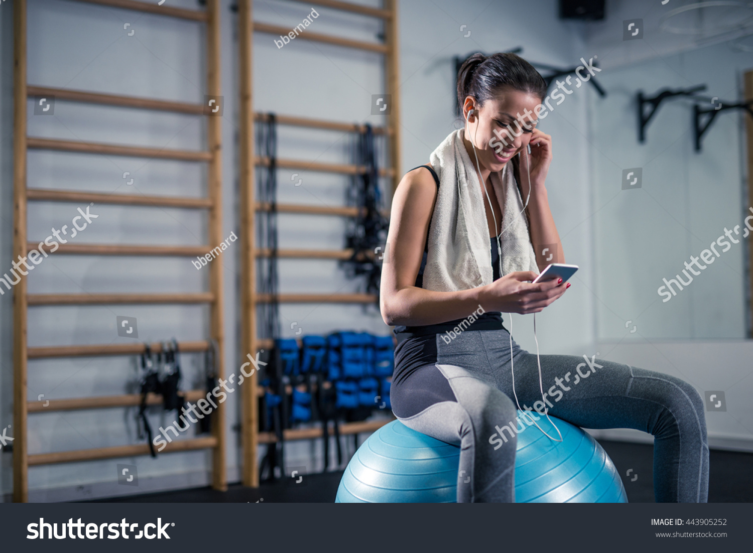 Woman listening to the music while sitting on a exercise ball in the gym.