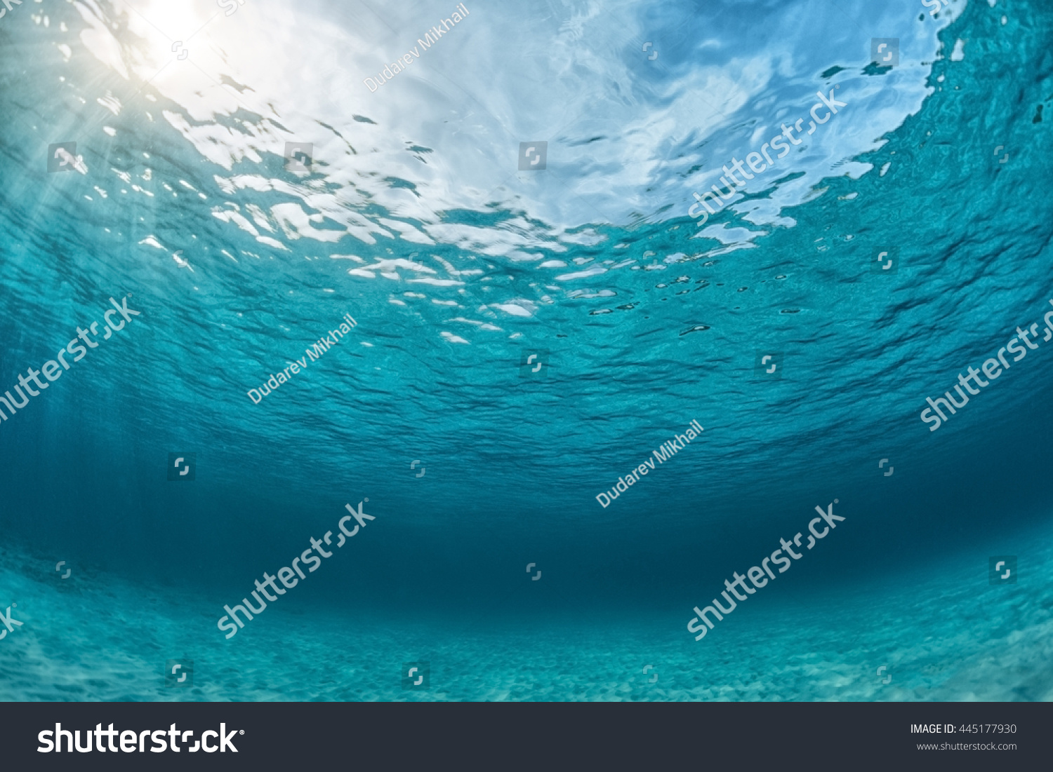 Underwater shoot of an infinite sandy sea bottom with clear blue water and waves on its surface