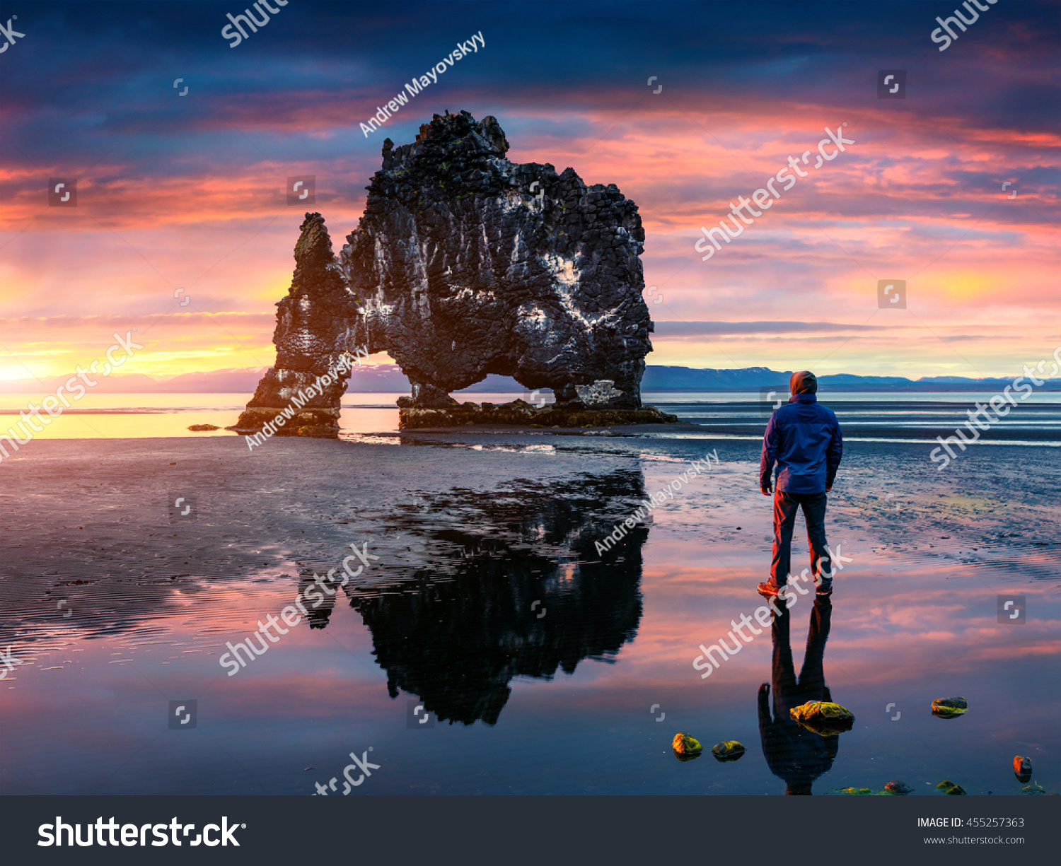 Man stands on the surface of water at fall of tide and and admiring of sunrise. Huge basalt stack Hvitserkur on the eastern shore of the Vatnsnes peninsula  Iceland  Europe. 