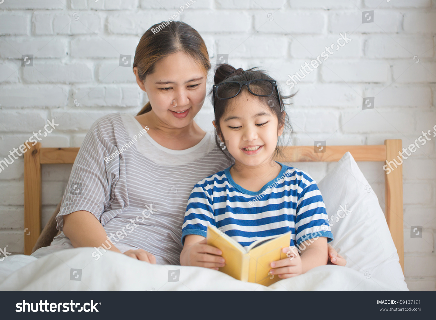 Happy Asian girl reading story book with her mother together