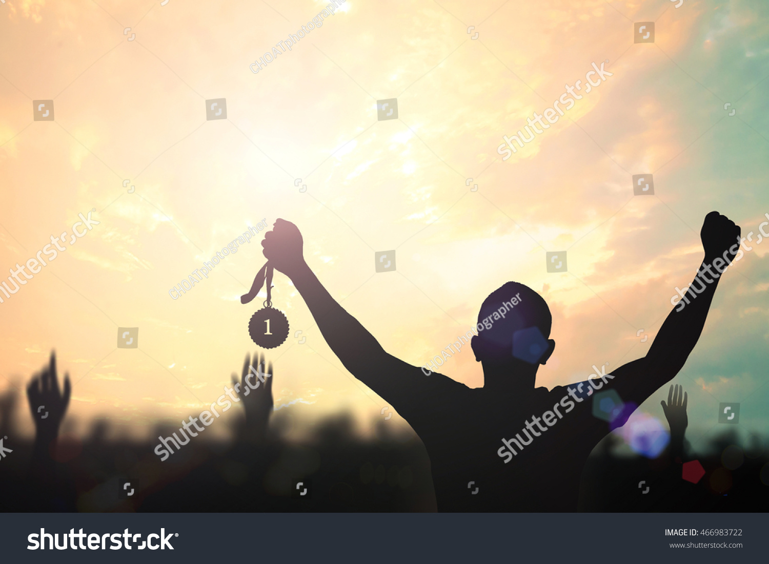 Winner concept: Silhouette champion hand holding gold medal reward against blurred sport stadium sunset background