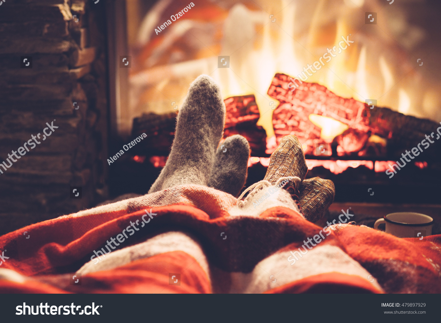 Cold fall or winter evening. People resting by the fire with blanket and tea. Closeup photo of feet in woolen socks. Cozy scene.