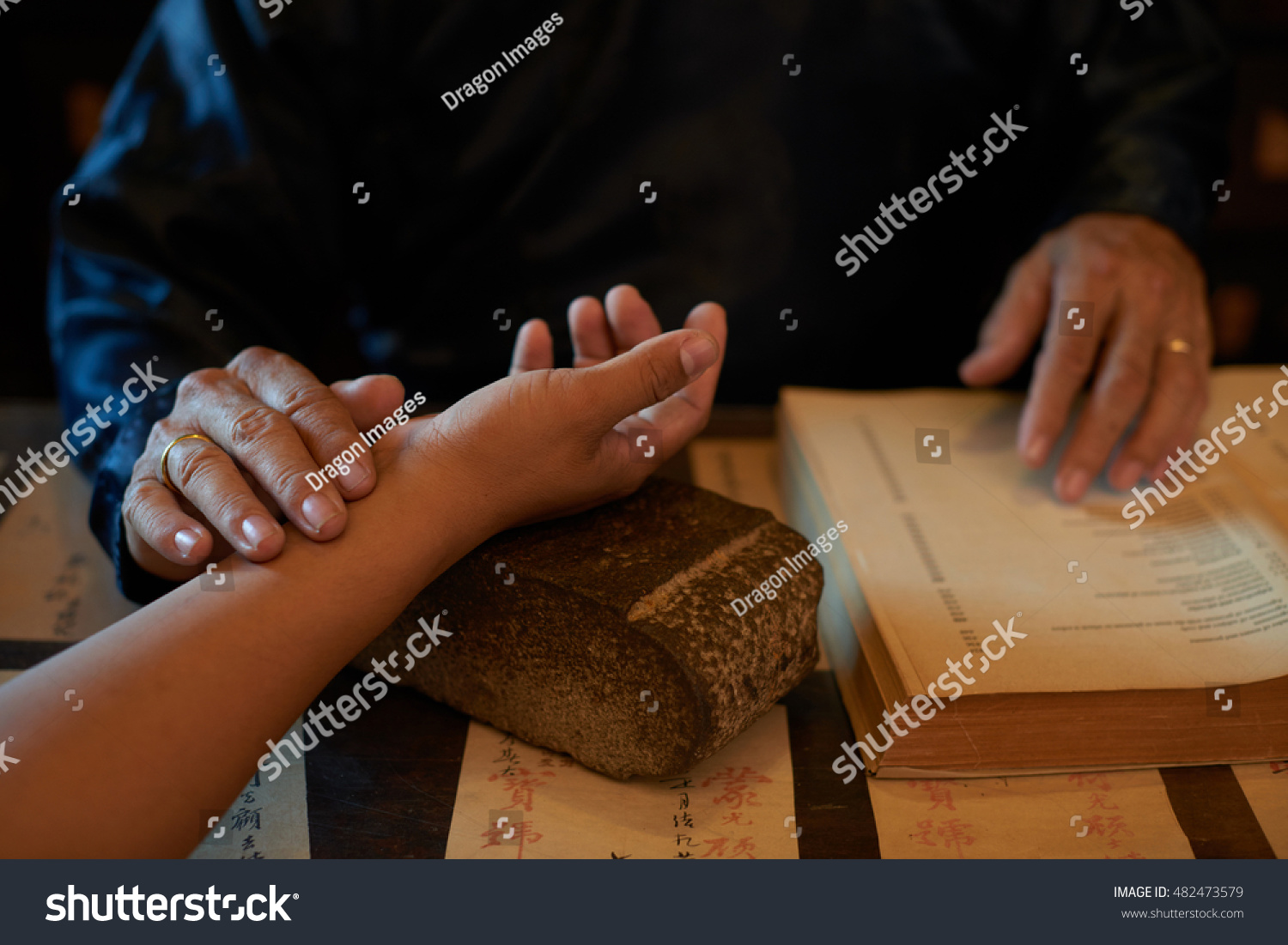 Asian traditional practitioner checking pulse of patient before treatment